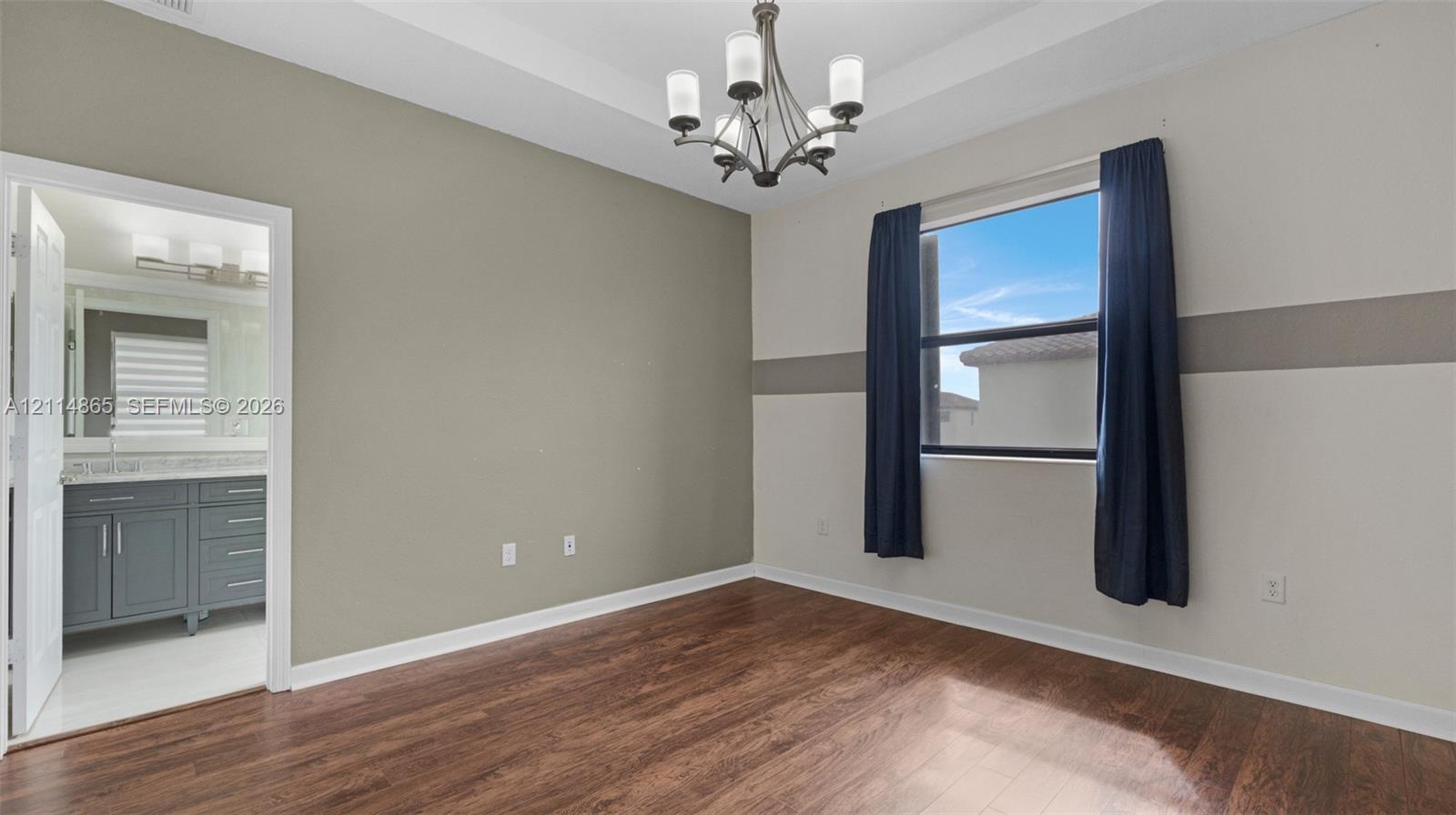 Room featuring wood-finish flooring, a tray ceiling, and a multi-arm chandelier
