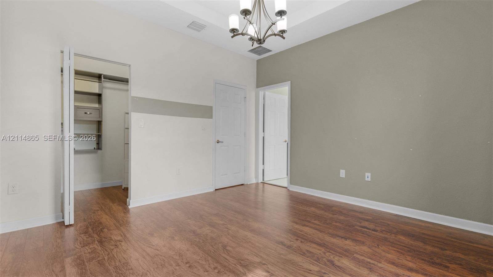 Room featuring wood-finish flooring, tray ceiling, multi-arm chandelier, and built-in closet shelving