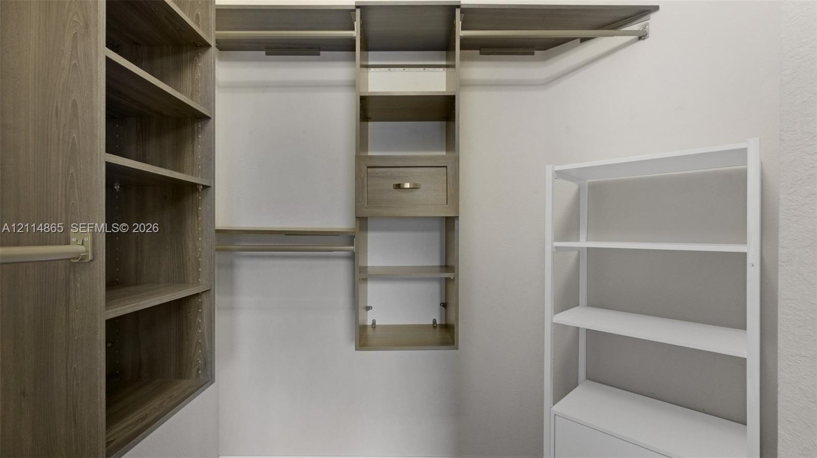 Custom closet organization system featuring wood-finish shelving, integrated clothing rods, and a central drawer unit with metallic hardware