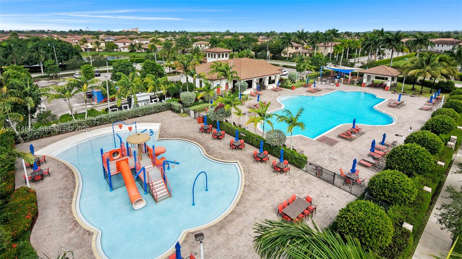 Community recreation area featuring a large swimming pool, splash pad with water play structures, paved deck, and a clubhouse