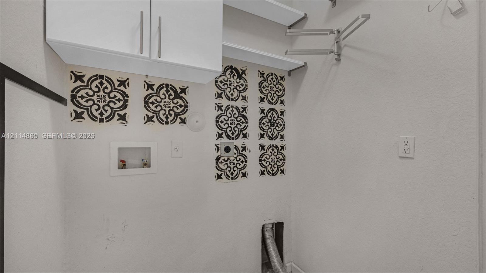 Utility area featuring white overhead cabinetry, open shelving, decorative tile accents, and a retractable wall-mounted garment rack
