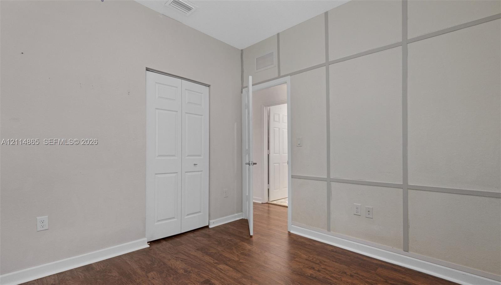 Room featuring wood-finish flooring, decorative wall molding, and a bi-fold closet door