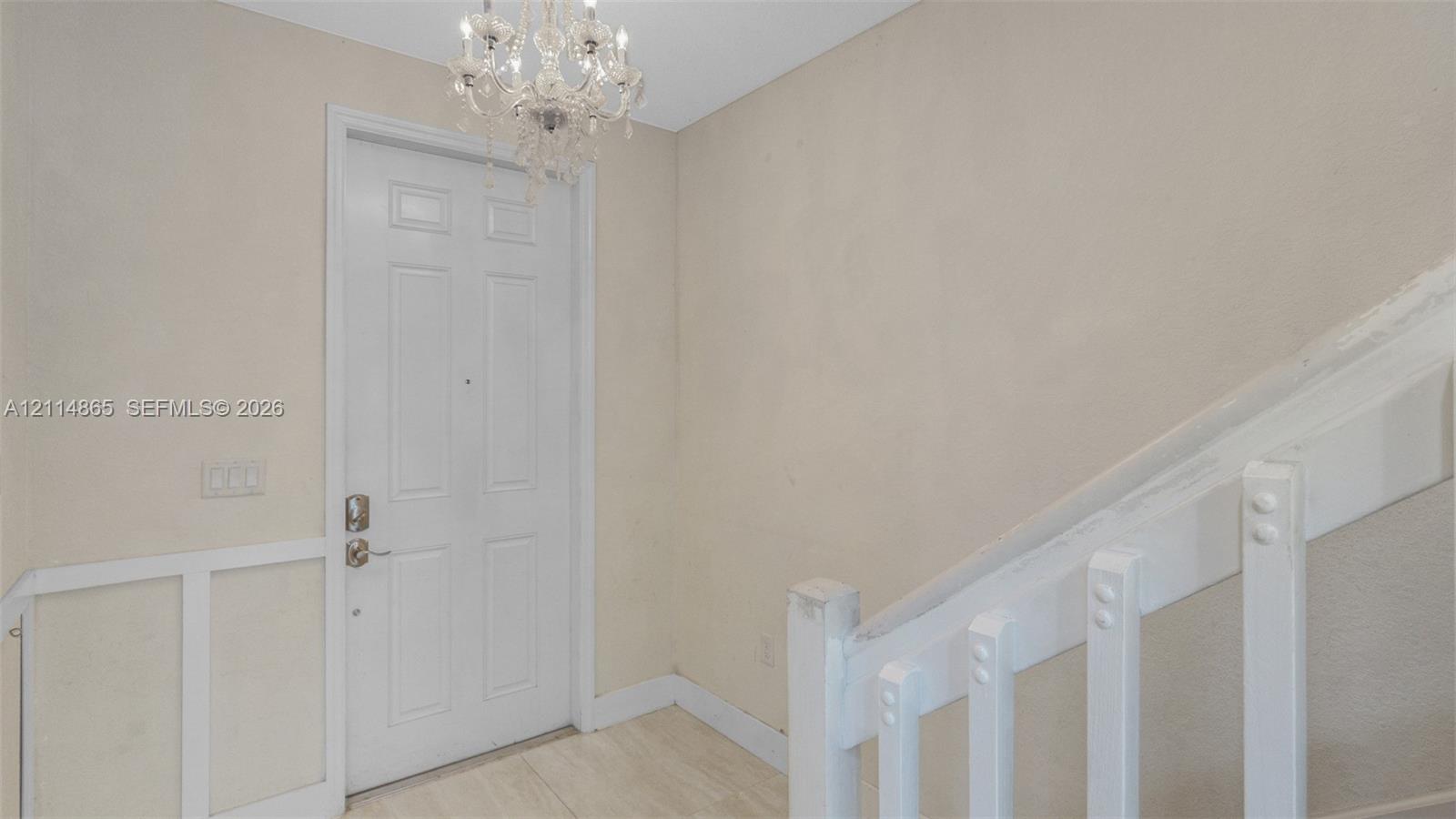 Entryway featuring a white paneled door, crystal-style chandelier, light-toned flooring, and a white staircase with a wooden railing and vertical balusters