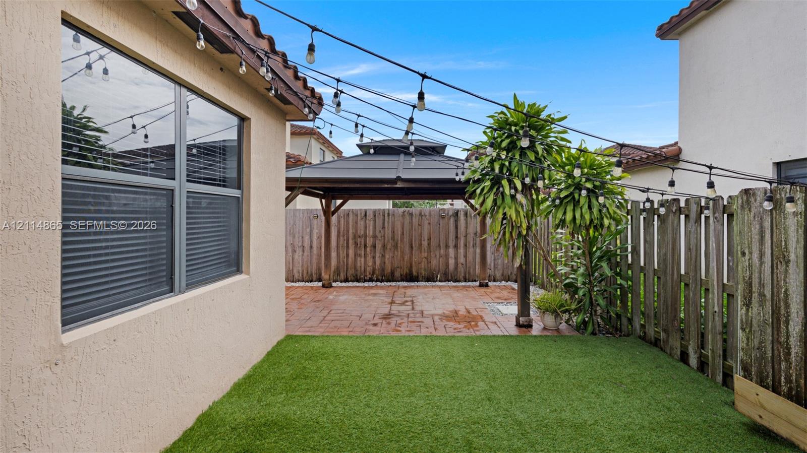 Private backyard featuring artificial turf, a paved patio, a covered wooden gazebo, and perimeter wood fencing