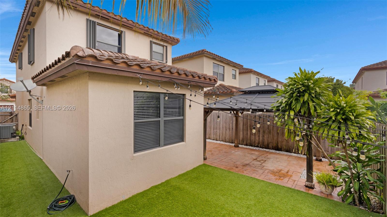 Stucco exterior with a tile roof, paved patio area, and synthetic turf lawn