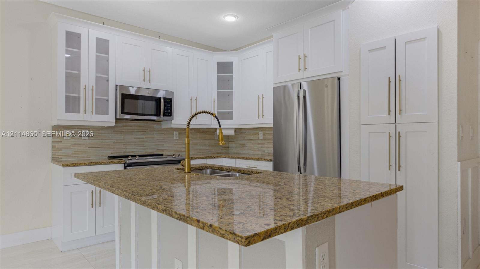 Kitchen featuring white shaker-style cabinetry, stone countertops, stainless steel appliances, a center island, and a gold-tone faucet