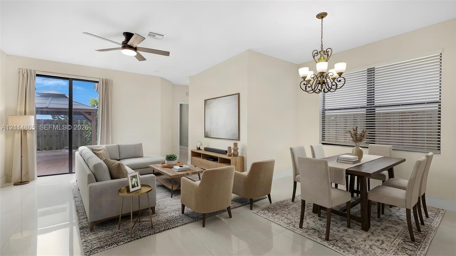Virtually staged. Open-concept floor plan featuring light-toned flooring, an ornate multi-arm chandelier, a ceiling fan with integrated lighting, and glass sliding doors