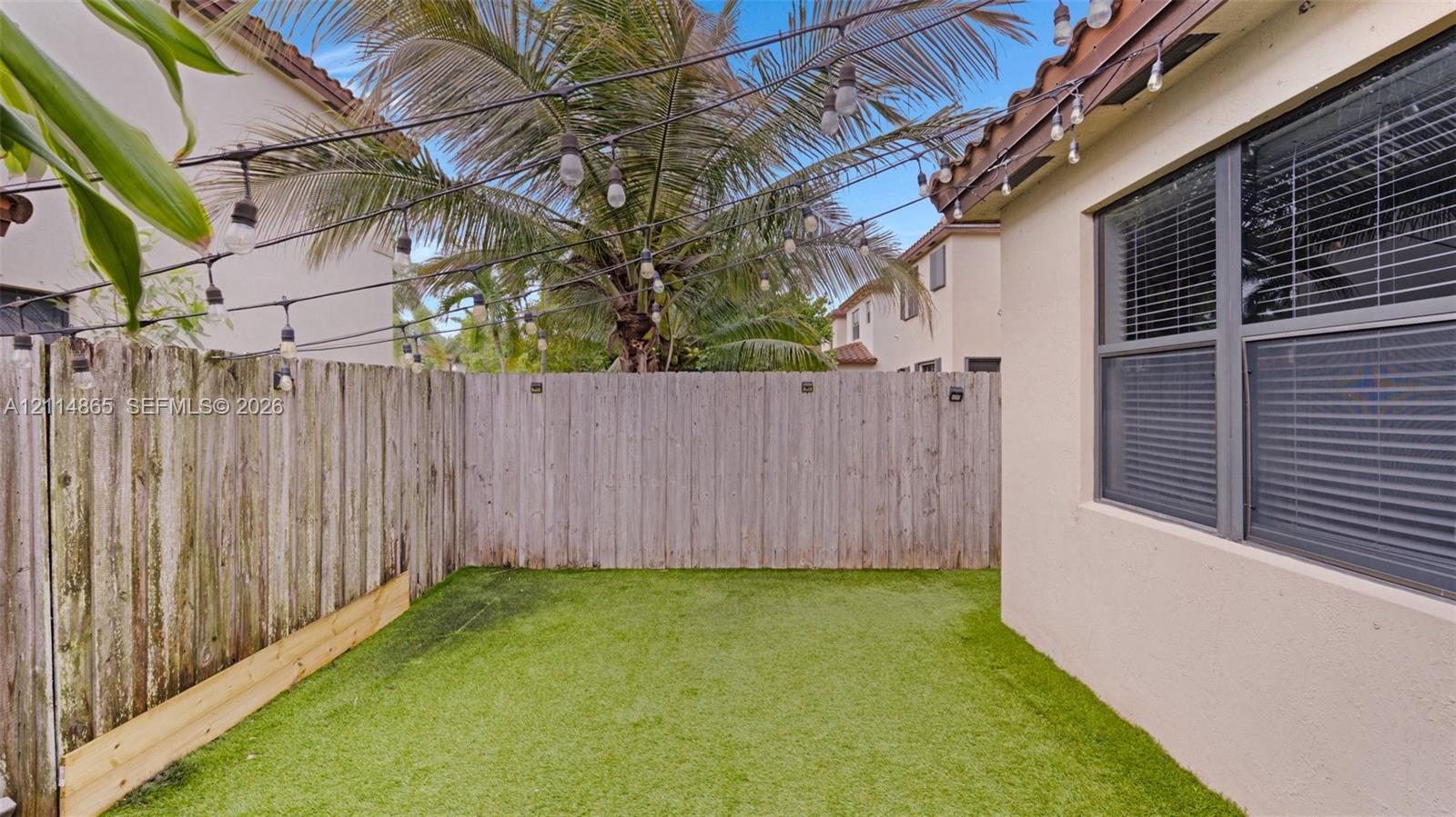 Outdoor space featuring artificial turf, wood fencing, and overhead string lighting