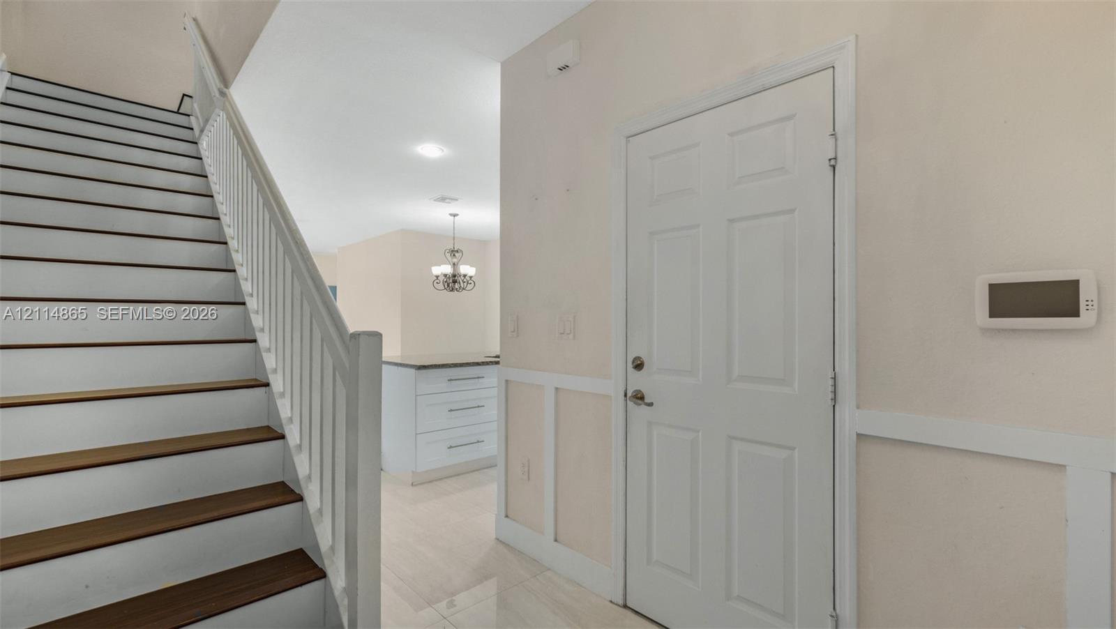 Interior entry featuring a staircase with wood-finish treads and white balusters, wainscoting wall paneling, and tile flooring