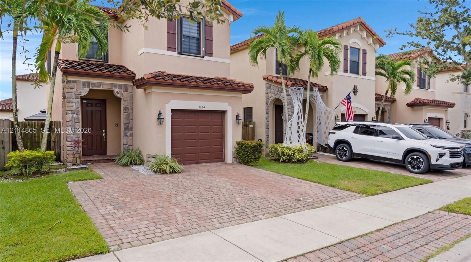 Two-story exterior featuring stucco siding, stone veneer accents, multi-tonal brick paver driveway, and a clay tile roof
