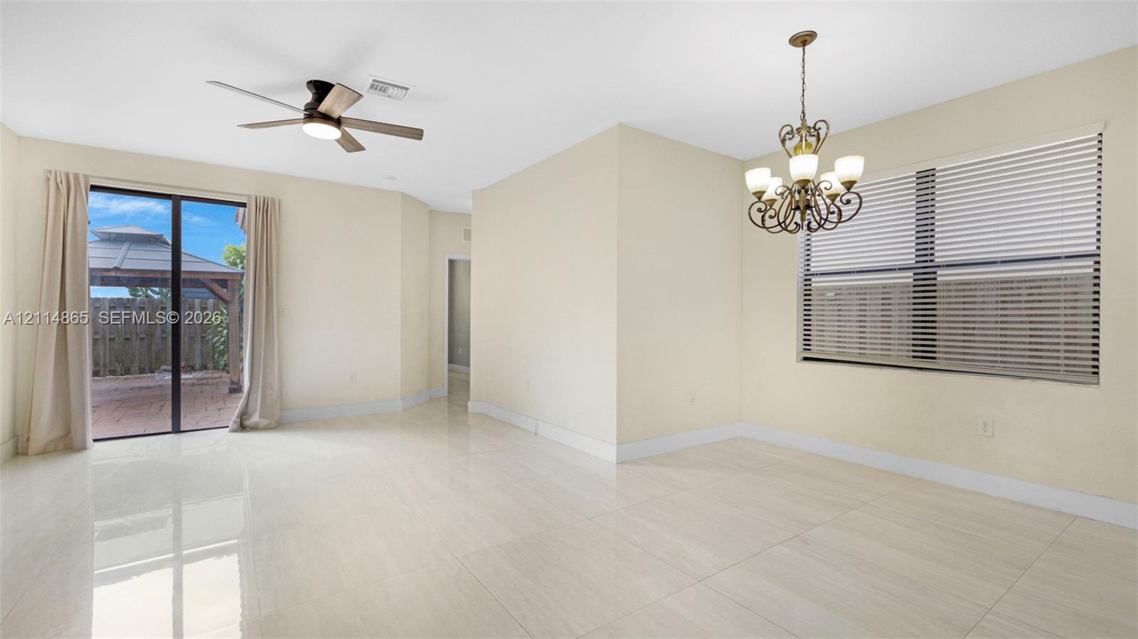 Open-concept interior featuring large-format tile flooring, a multi-arm chandelier, ceiling fan with integrated lighting, and glass sliding doors