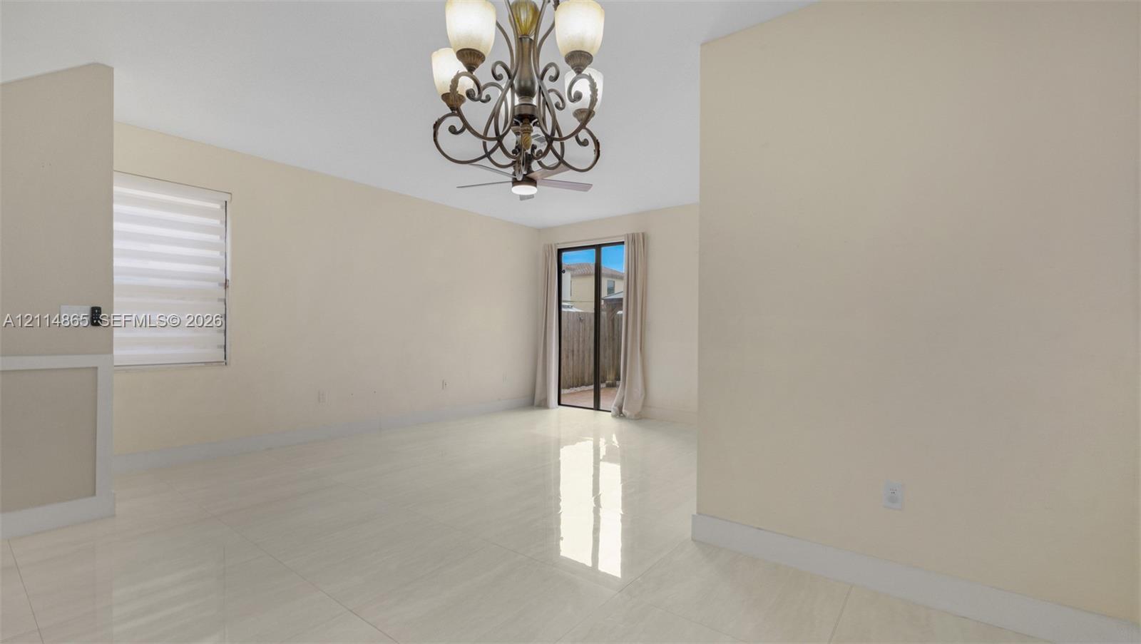 Open-concept room featuring polished tile flooring, decorative multi-arm chandelier, ceiling fan, sliding glass door, and adjustable window blinds