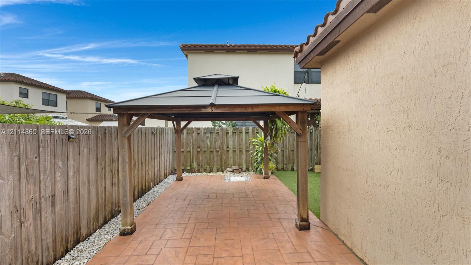 Covered outdoor gazebo featuring a metal roof and wood-frame structure set upon a stamped concrete patio, enclosed by a wood privacy fence