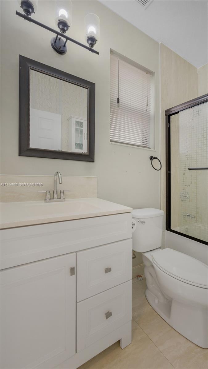 1st floor bathroom! Perfect guest bath/in-law space White vanity cabinet with a stone-surface countertop, rectangular framed wall mirror, three-light vanity fixture, and shower enclosure with a dark-finish frame