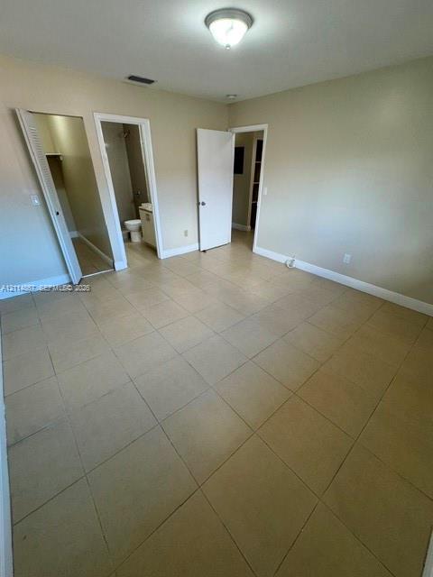 Neutral-toned interior space featuring large-format tile flooring, a flush-mount ceiling light fixture, and multiple access points including a walk-in closet and internal doorway
