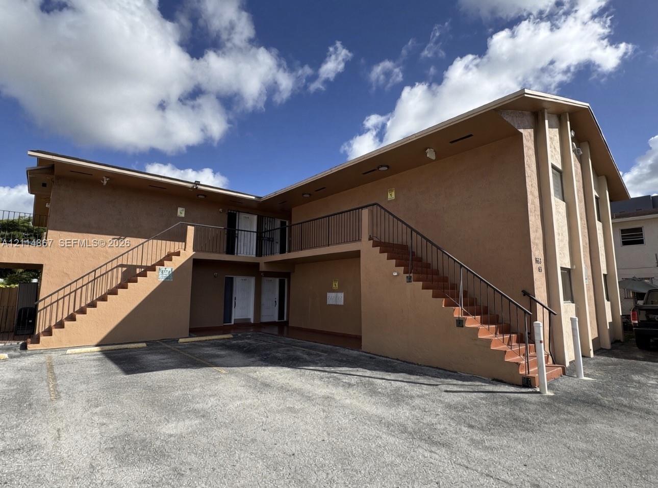 Two-story exterior featuring stucco siding, multiple external staircases with metal railings, a paved parking area, and recessed soffit lighting