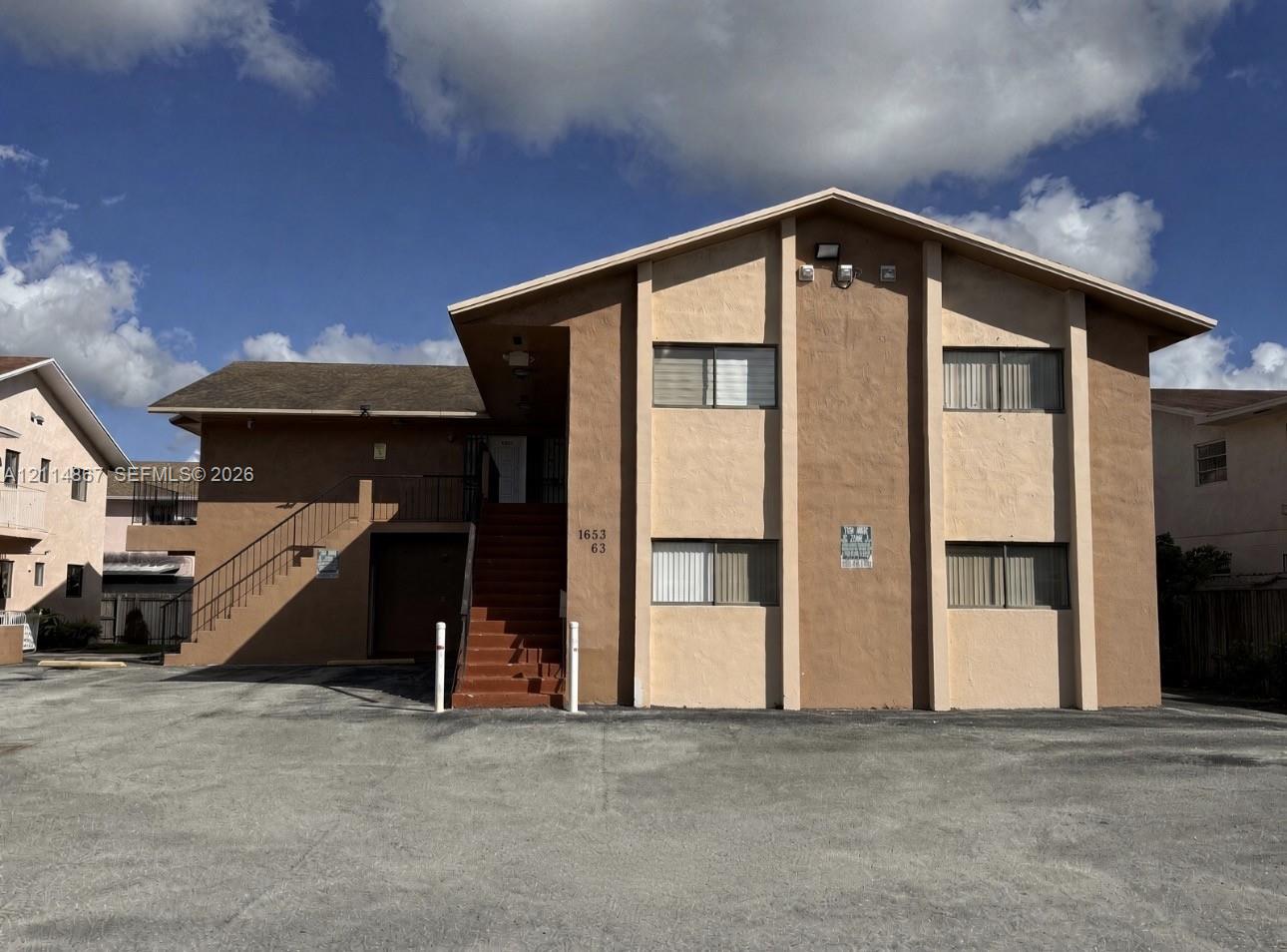 Multi-story exterior featuring a stucco facade, gable roofline, concrete parking area, and an external staircase with metal railing