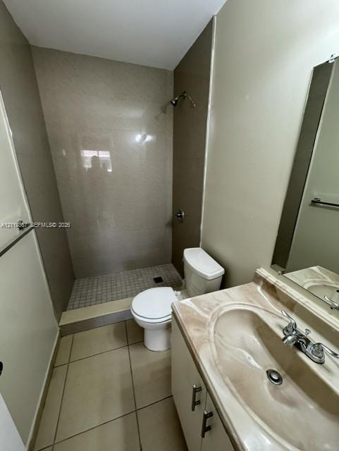 Bathroom featuring a vanity with a molded countertop and integrated sink, walk-in shower with tile surround, mosaic tile shower floor, and large-format floor tiling