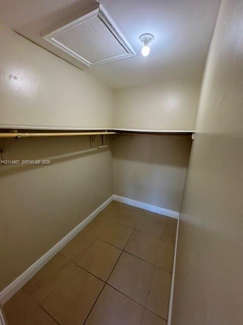 Storage space featuring tile flooring, built-in shelving, and a garment rod