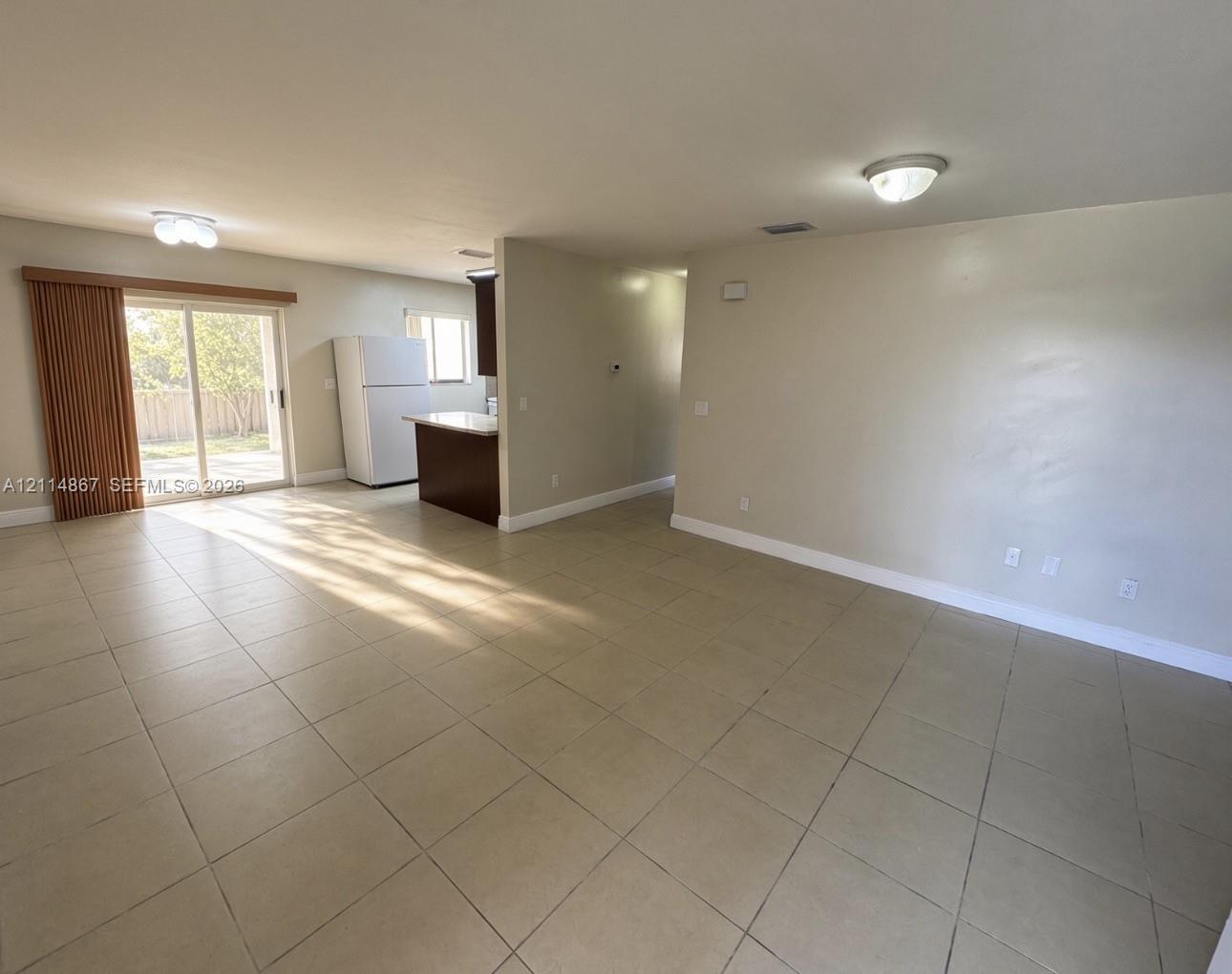 Open living area featuring neutral tile flooring, sliding glass doors, built-in kitchen cabinetry with a peninsula, and recessed overhead lighting Open living area featuring neutral tile flooring, sliding glass doors, built-in kitchen cabinetry with a peninsula, and recessed overhead lighting