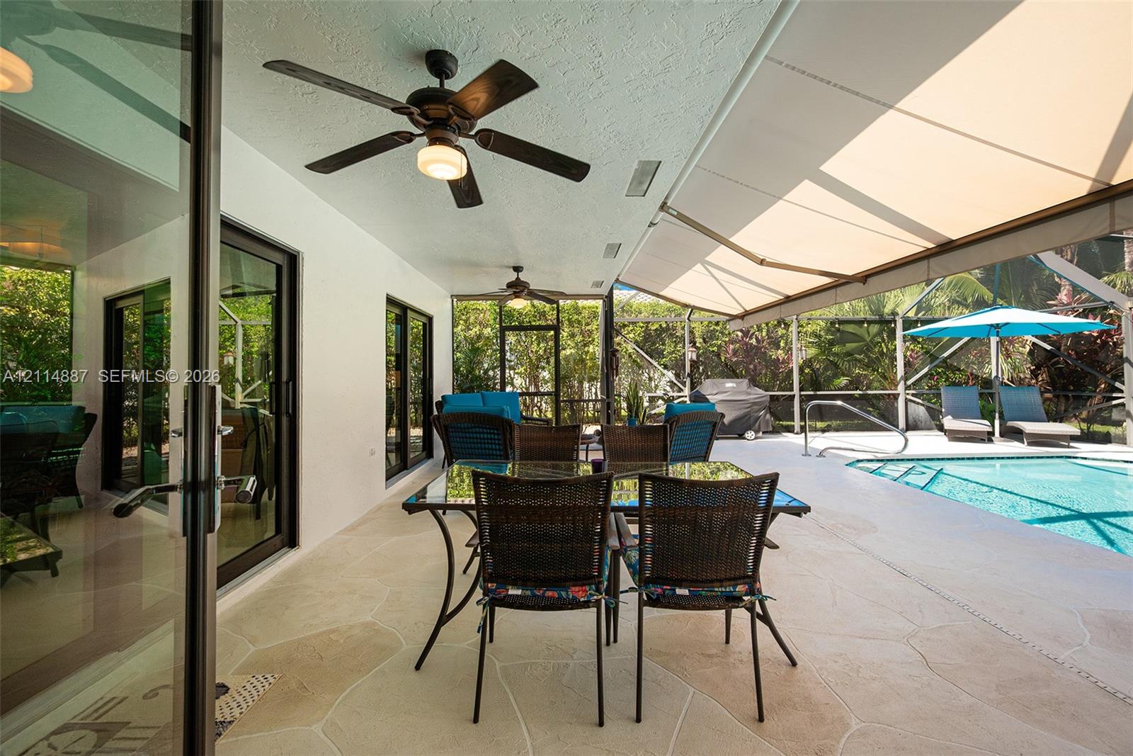Covered screened-in lanai featuring stone-tile flooring, dual ceiling fans, a retractable fabric awning, and a built-in swimming pool