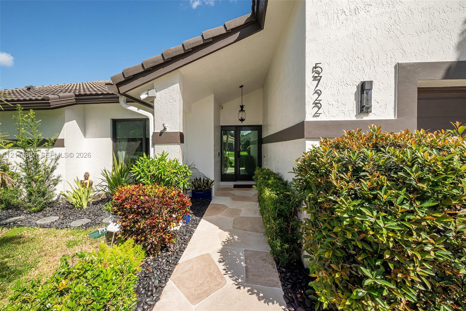 Stucco exterior featuring tile roofing, a paved stone walkway, and a glass-paneled entry door