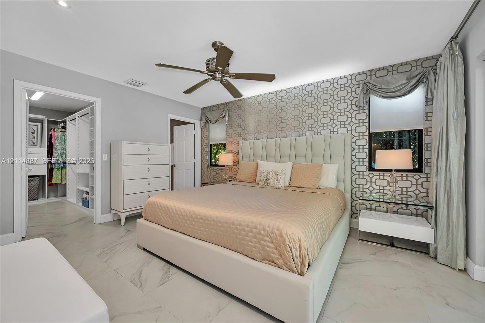 Large-format tile flooring, patterned wallpaper accent wall, integrated ceiling fan, recessed lighting, and walk-in closet with built-in shelving