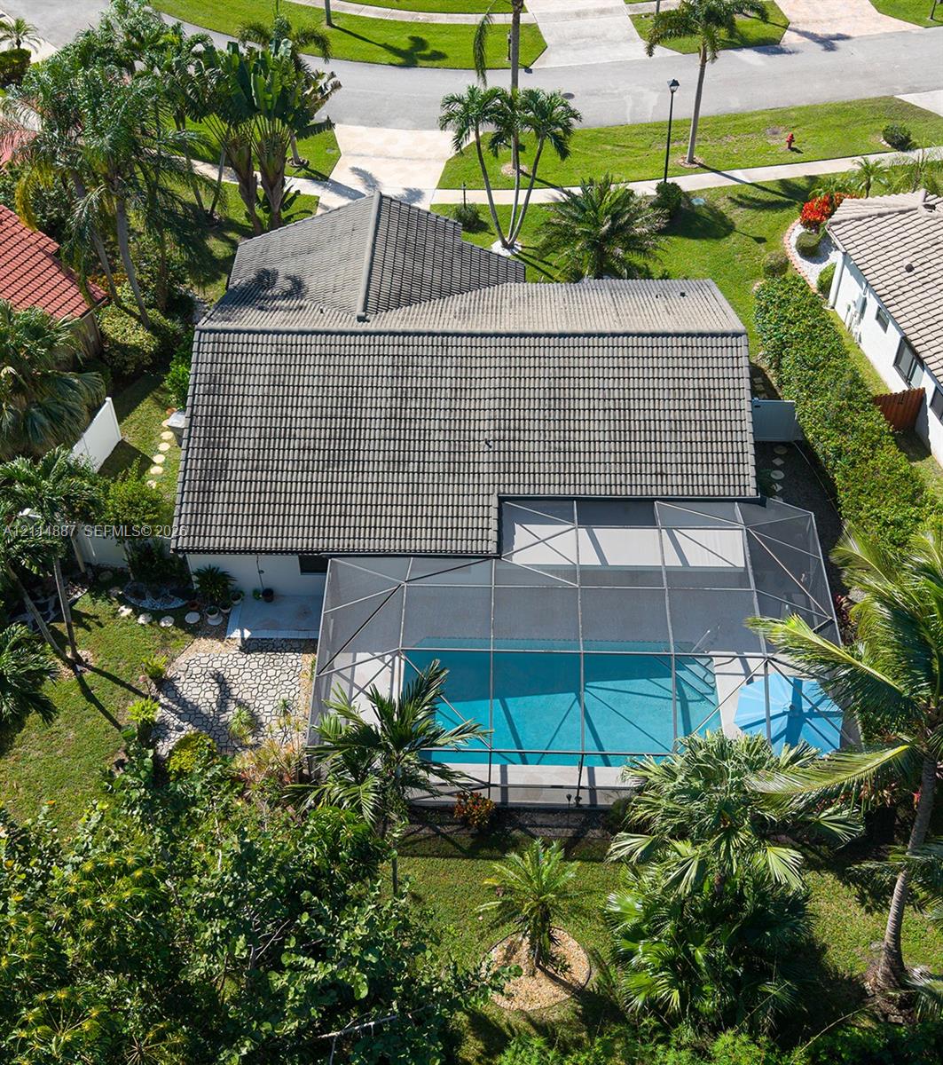 Tile roof structure featuring a screened-in swimming pool enclosure, paver patio, and landscaped perimeter with mature palm trees