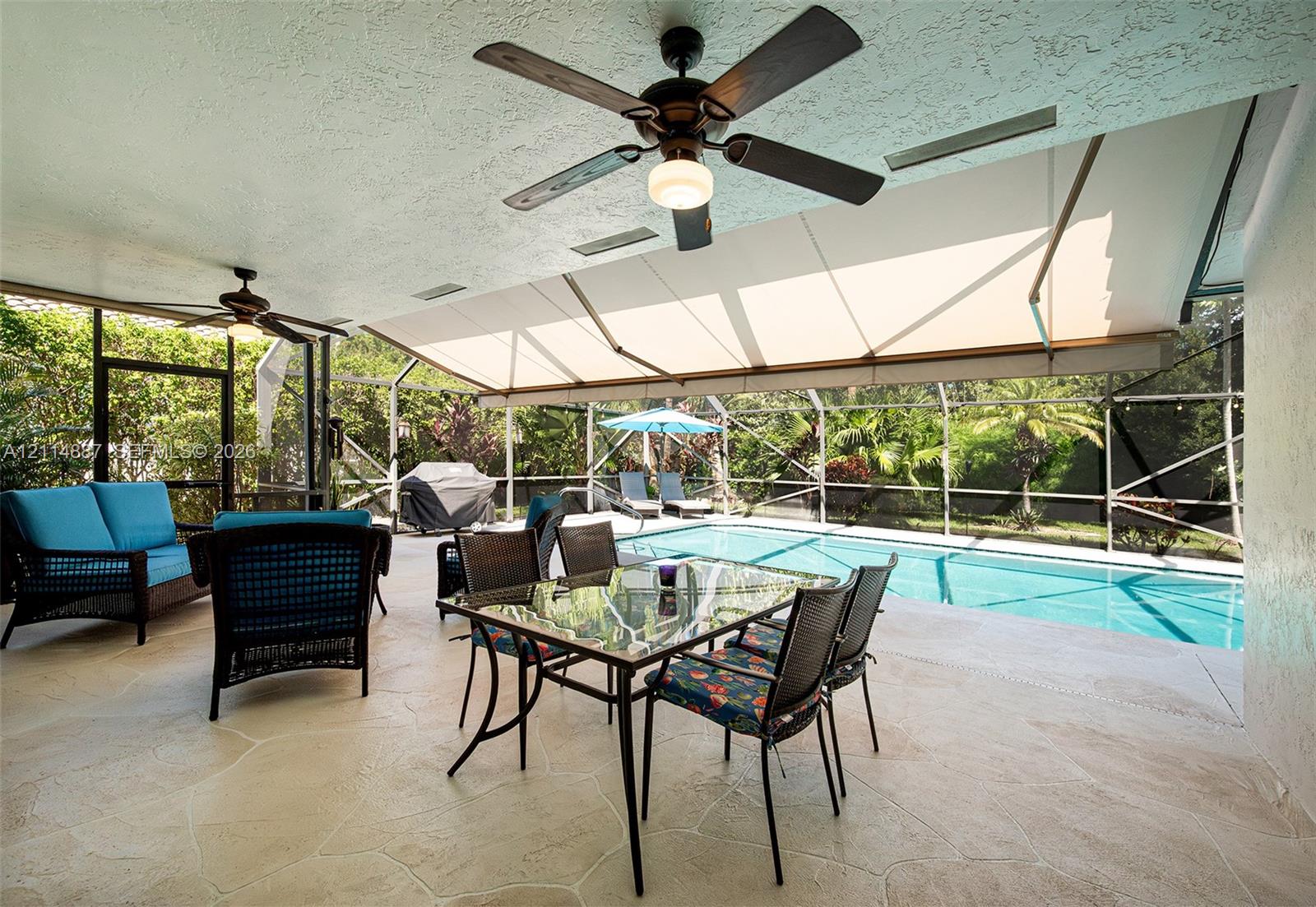 Covered outdoor patio featuring flagstone flooring, two ceiling fans, a retractable awning, and a screened enclosure surrounding the swimming pool