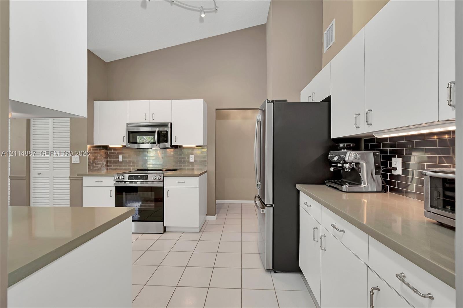 Kitchen featuring white cabinetry, solid surface countertops, stainless steel appliances, dark subway tile backsplash, and vaulted ceilings