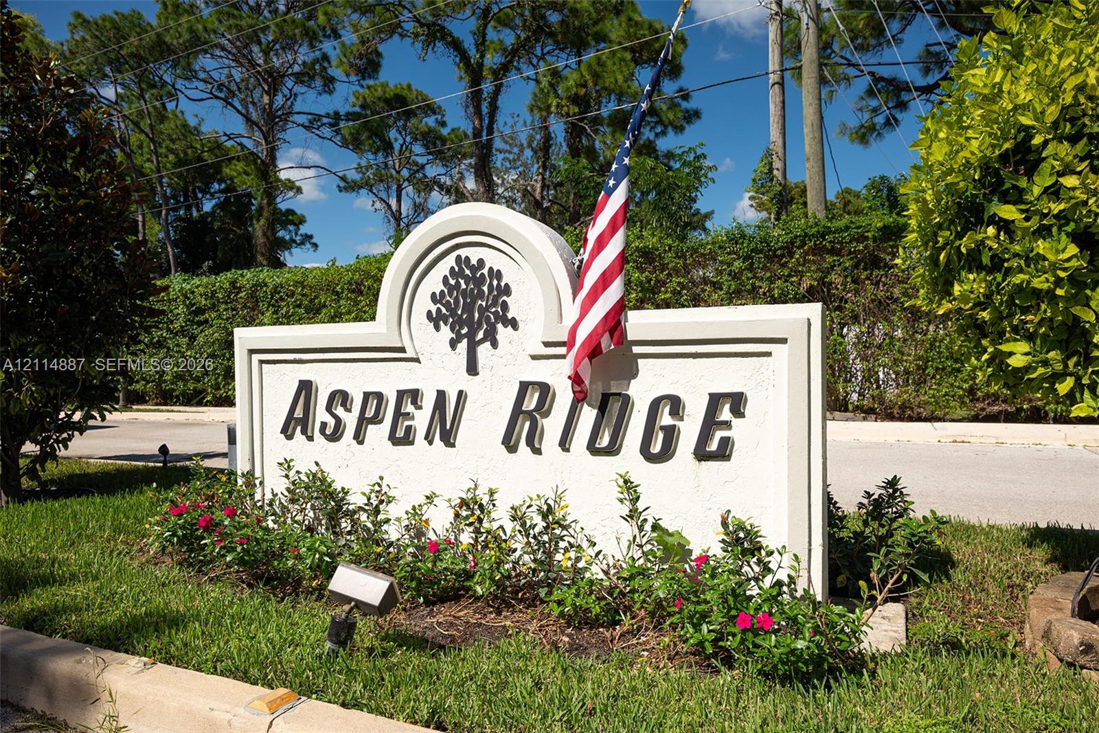 Custom monument signage featuring an arched profile, dimensional lettering, and integrated landscape beds with mature greenery and flowering shrubs