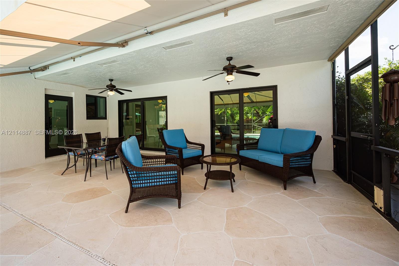 Covered patio featuring flagstone-style flooring, screen enclosure, dual ceiling fans, and sliding glass doors
