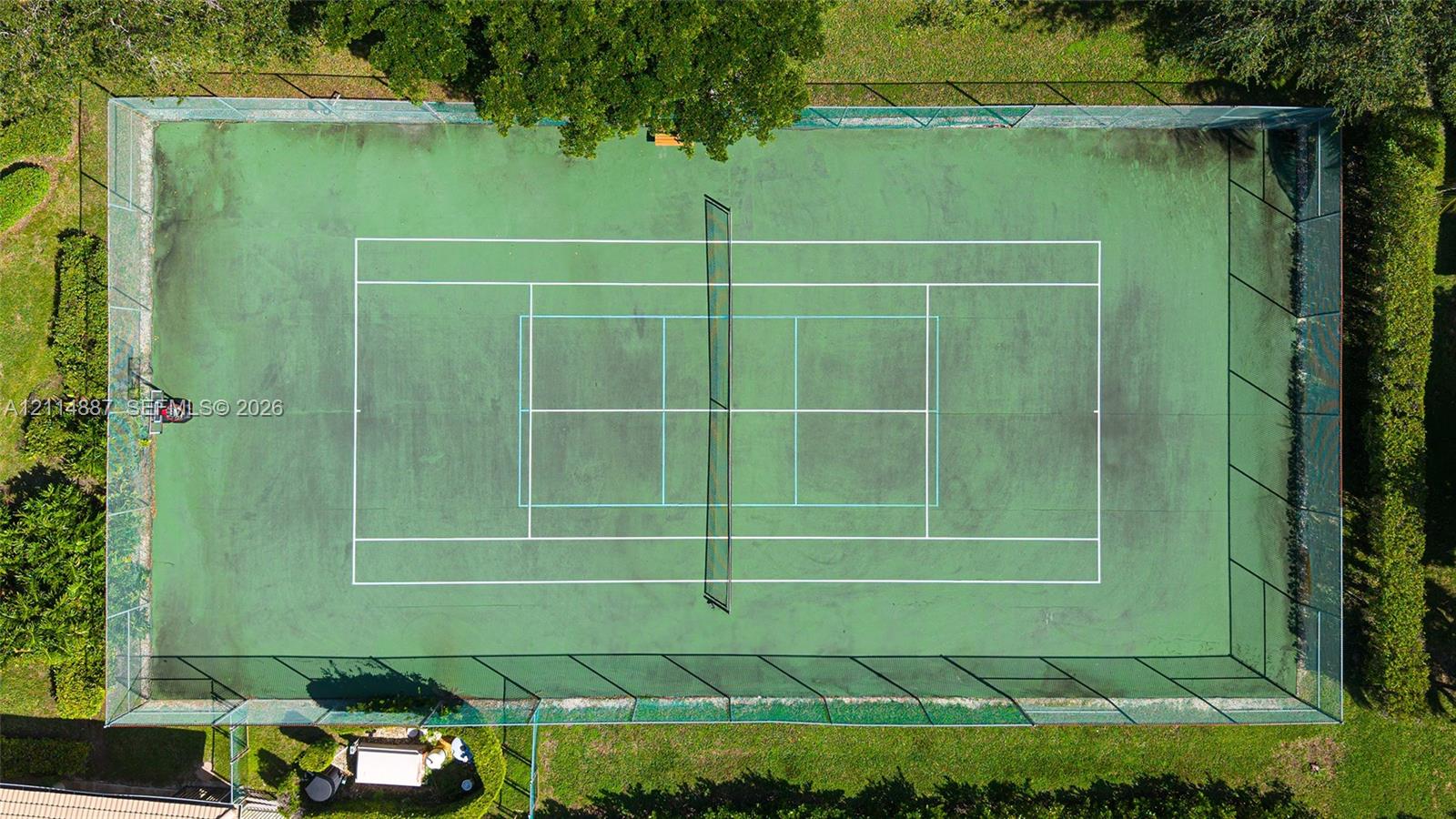 Private tennis court featuring a fenced perimeter and surrounding mature landscaping