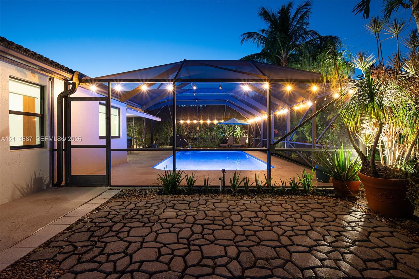 Screen-enclosed swimming pool with a paved deck, paver patio, and exterior string lighting