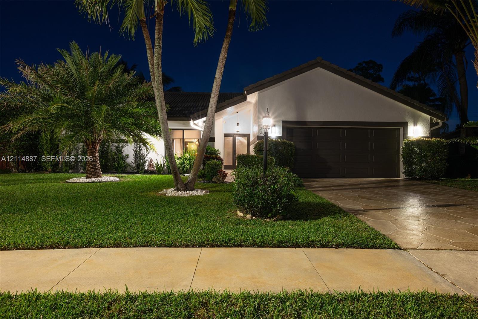 Single-story exterior featuring a stone-paver driveway, double-car garage, mature palm trees, and manicured landscaping