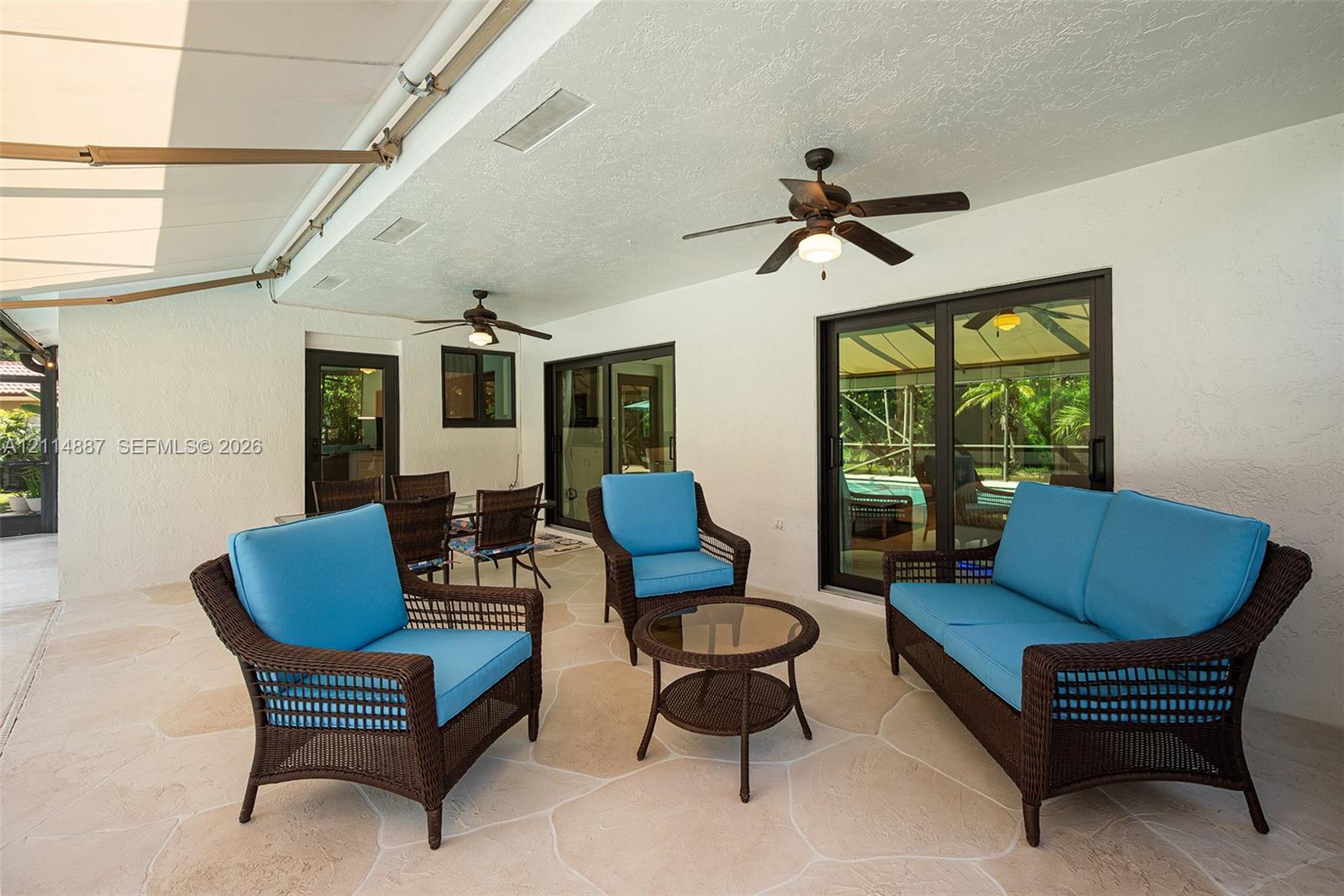 Covered patio featuring flagstone-style flooring, dual ceiling fans, a retractable exterior awning, and sliding glass doors