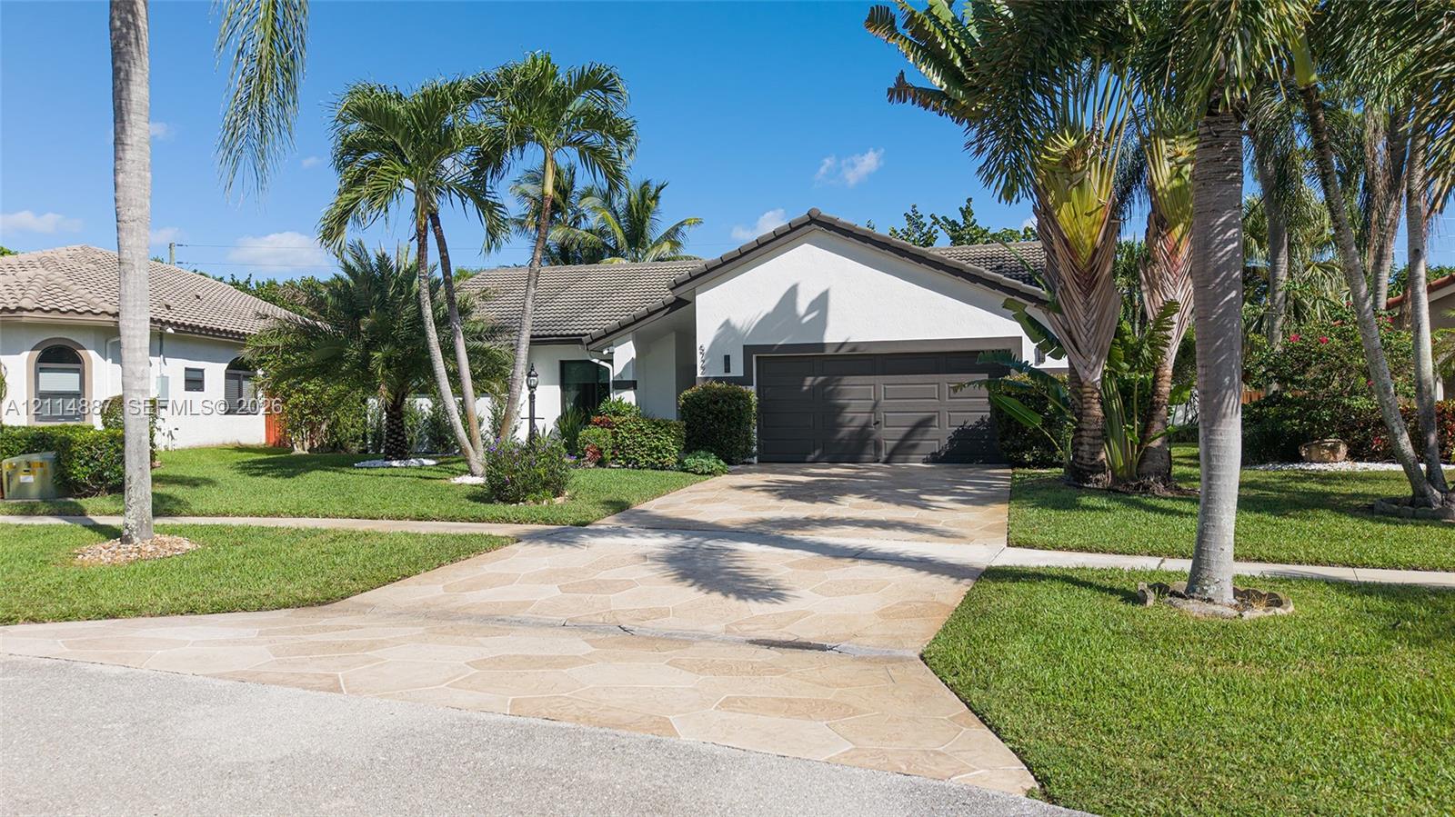 Stucco exterior with a multi-car garage, stone-paver driveway, and mature palm landscaping