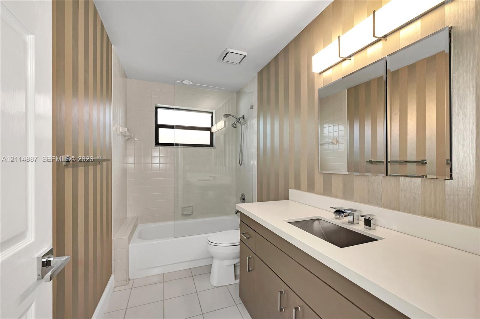 Bathroom featuring a vanity with a solid-surface countertop, integrated rectangular sink, wall-mounted medicine cabinet, frameless glass shower enclosure, and striped wall finish
