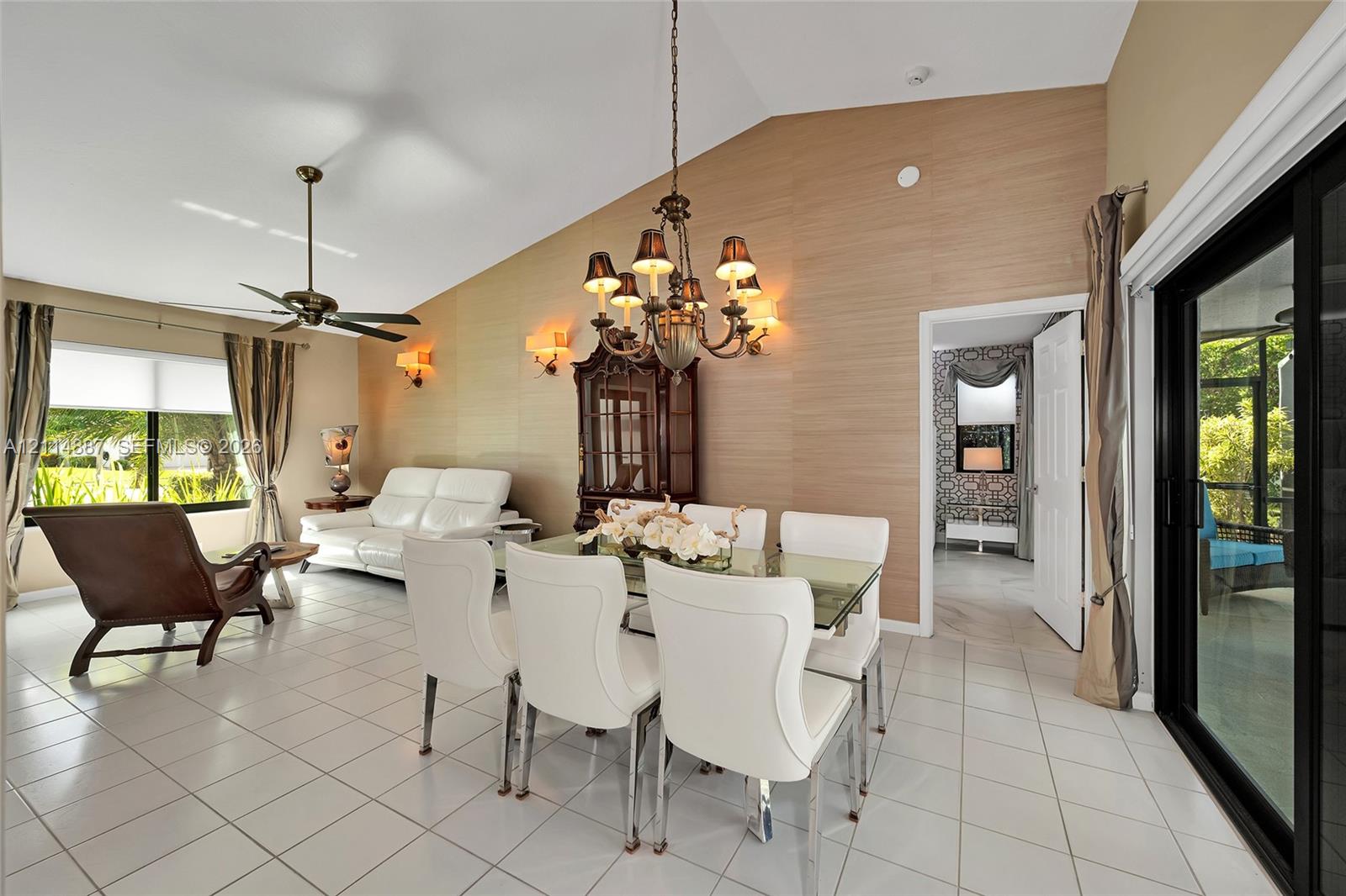Vaulted ceilings, feature wall with textured surfacing, multi-arm chandelier, ceiling fan, and sliding glass doors with exterior access