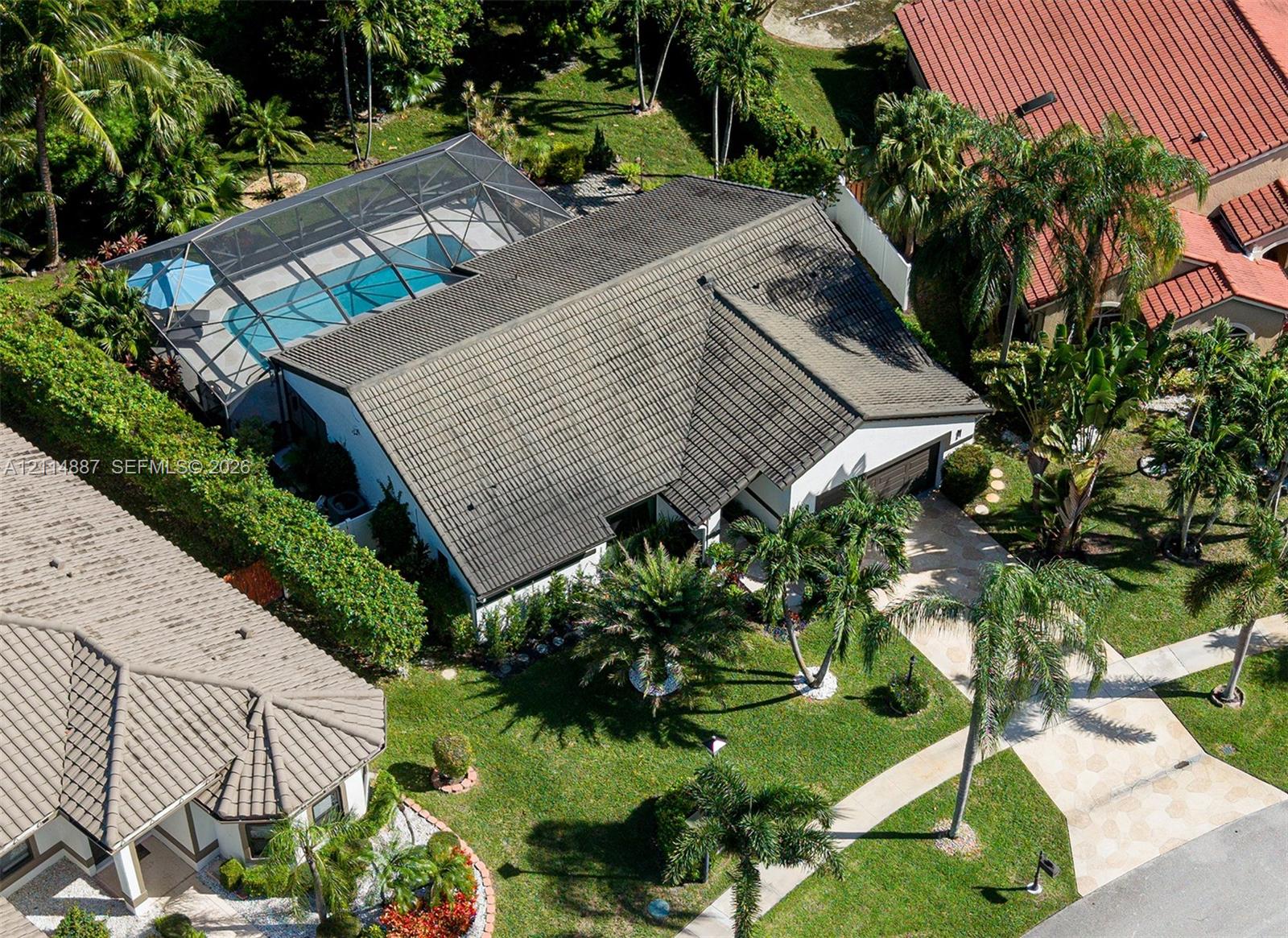 Aerial perspective of a residence featuring a screen-enclosed pool, tile roofing, a paved driveway, and mature palm landscaping