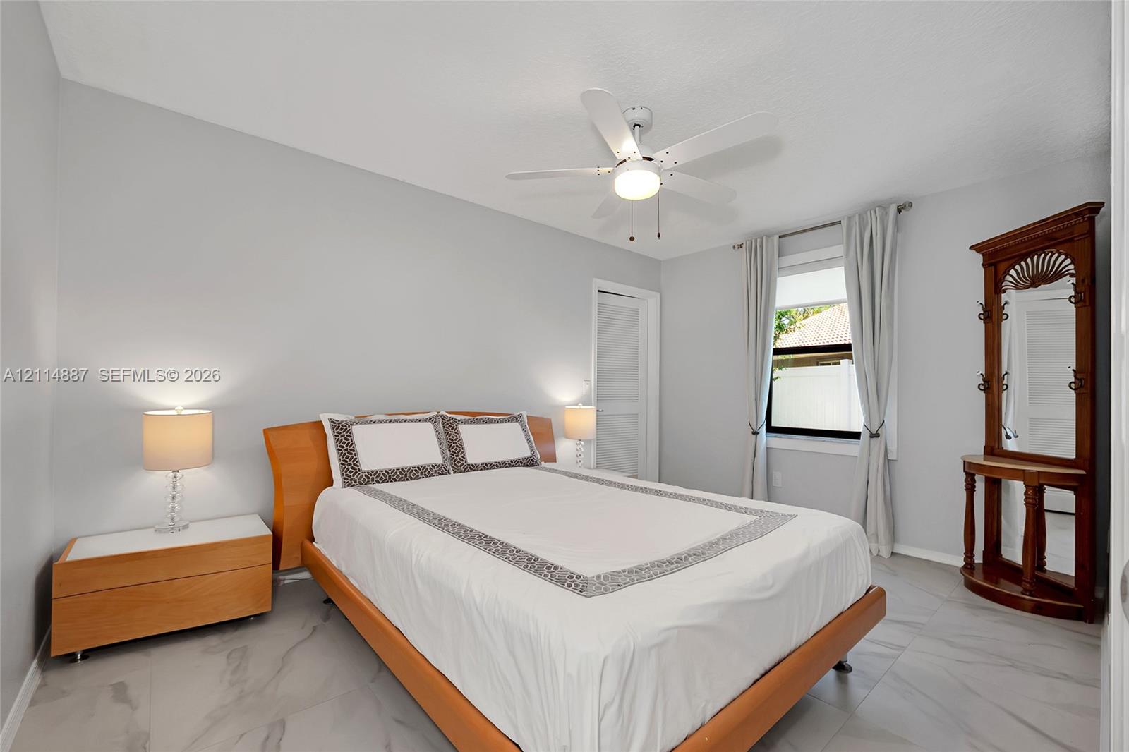 Neutral-toned room featuring large-format tile flooring, a white ceiling fan with integrated lighting, and a window with neutral drapery