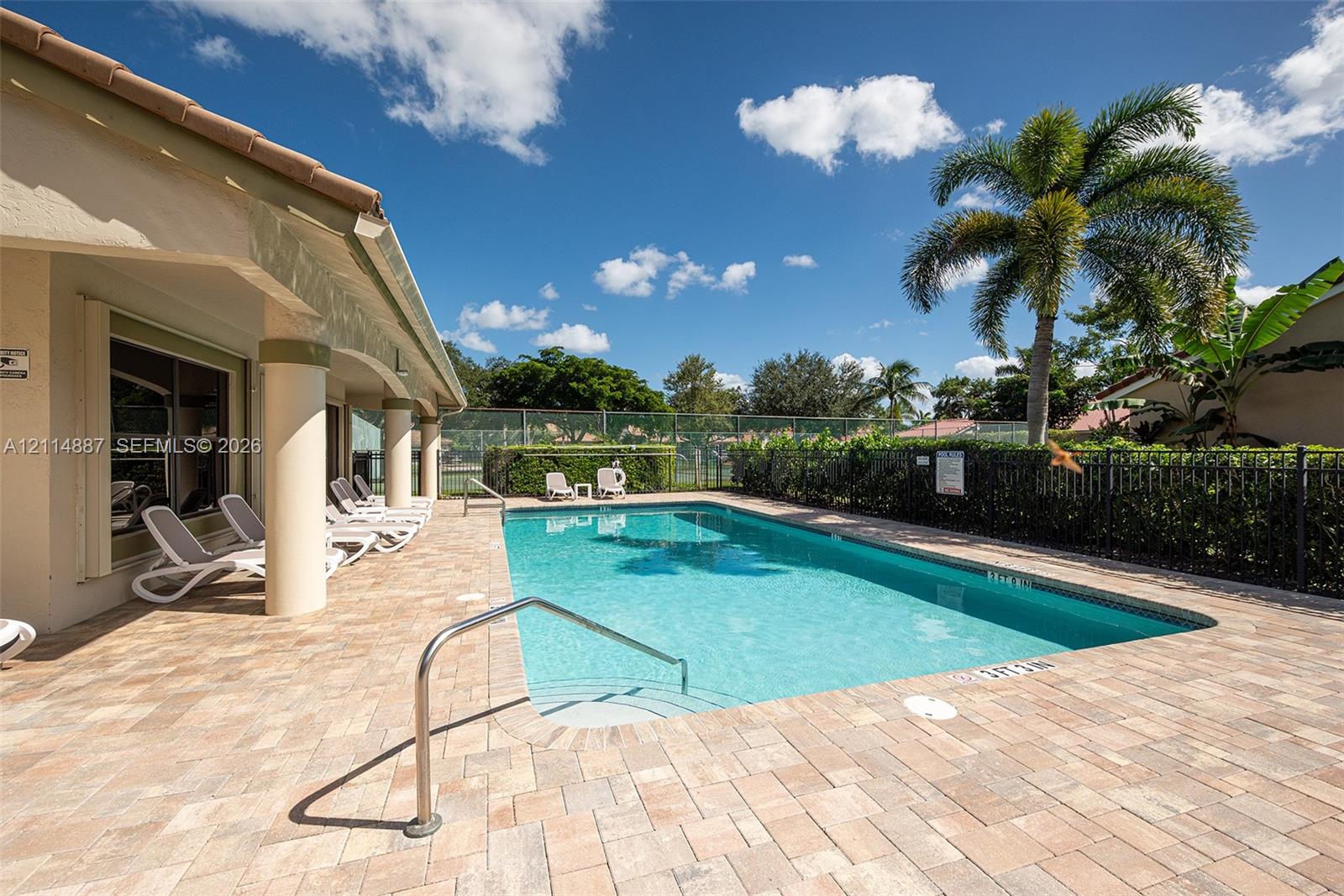 Outdoor swimming pool featuring a brick paver deck, covered patio with structural columns, and perimeter metal fencing