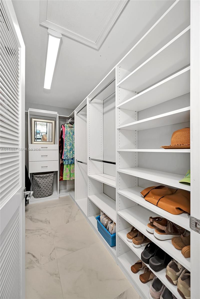Walk-in closet featuring floor-to-ceiling white built-in shelving, integrated dresser drawers, metal hanging rods, and large-format tile flooring