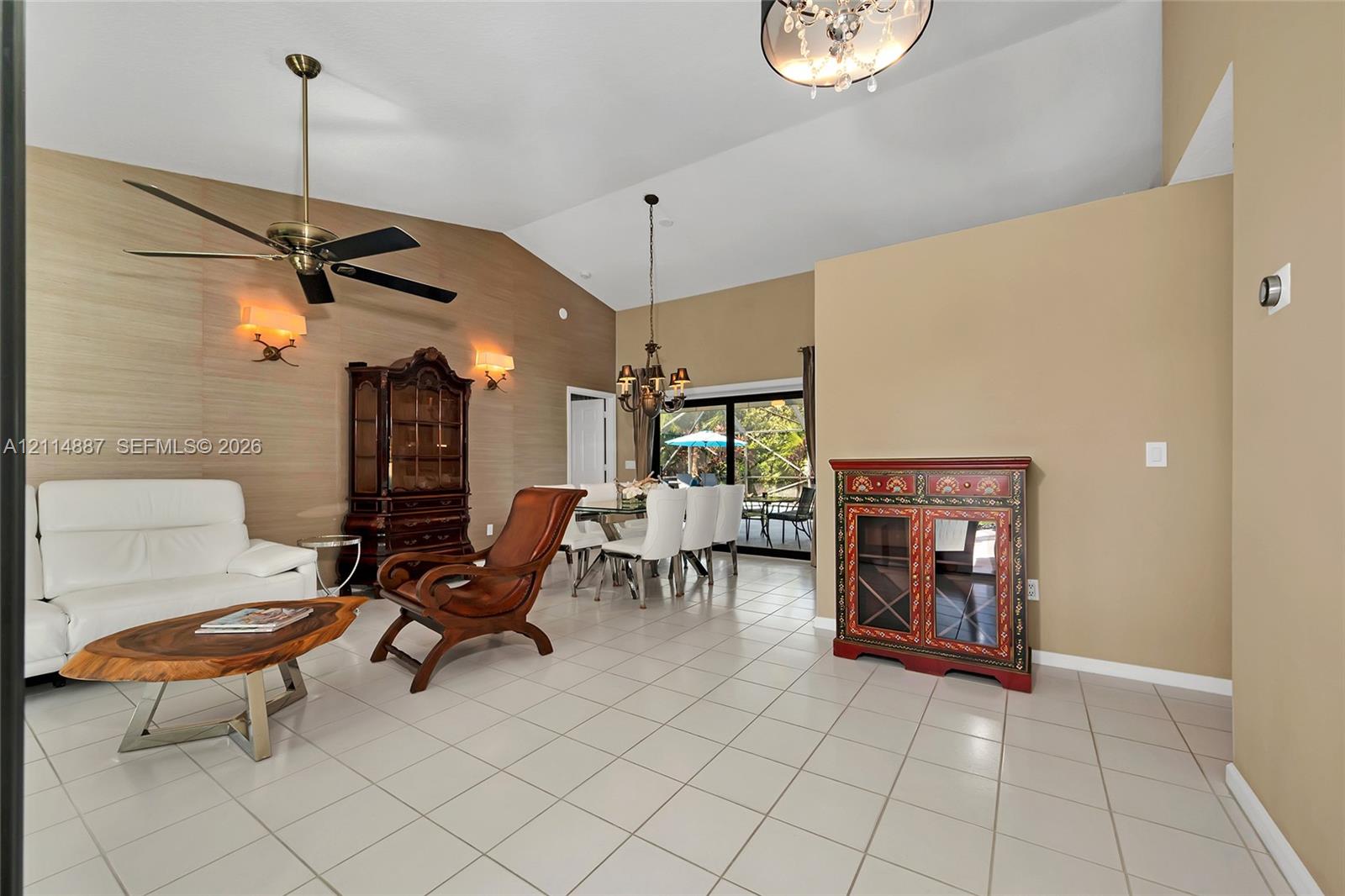 Vaulted ceilings, textured wall treatment, ceramic tile flooring, multi-arm chandelier, and sliding glass patio doors