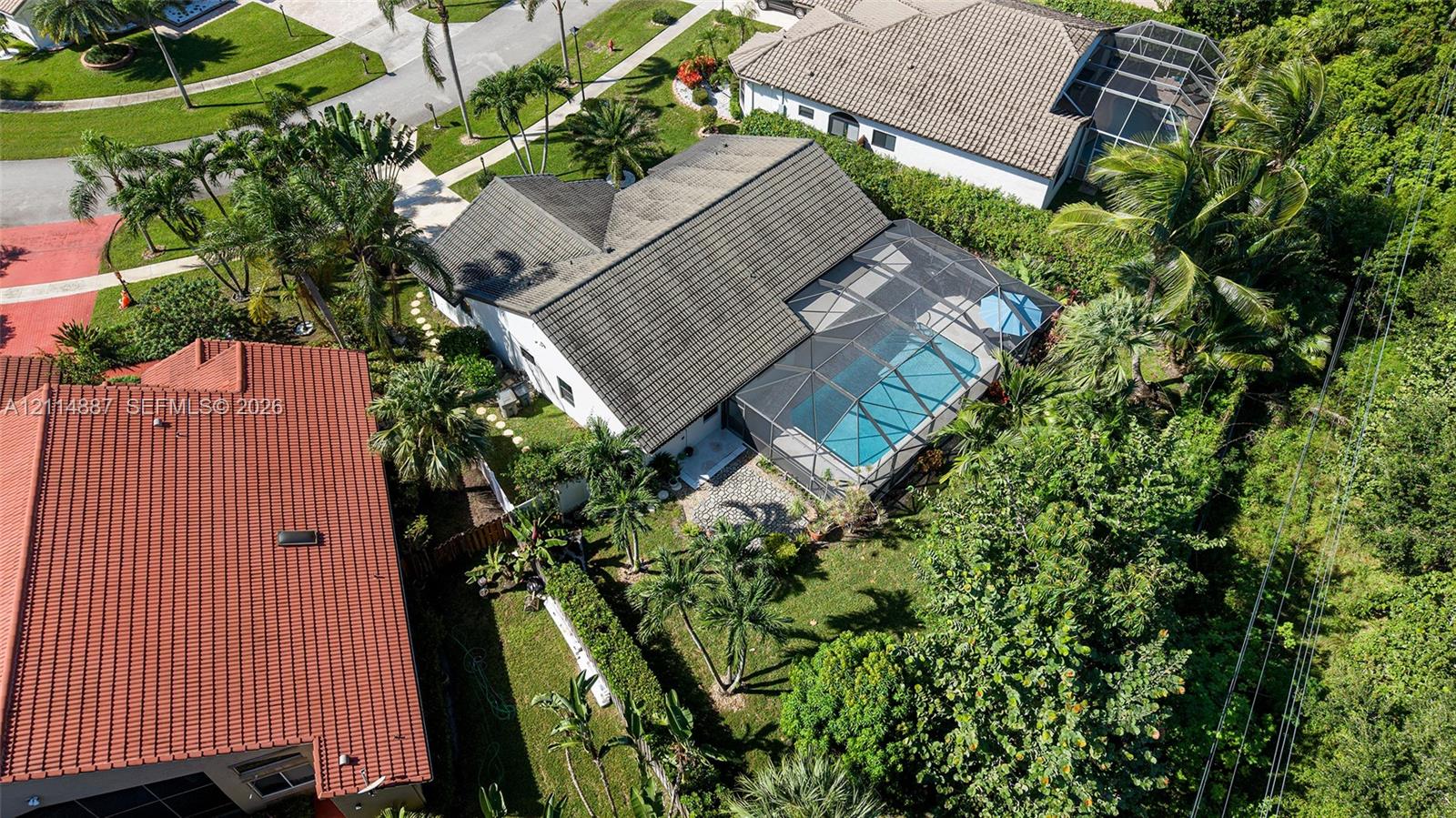 Aerial perspective of a property featuring a screened-in swimming pool, paved patio, lush landscaping, and mature palm trees