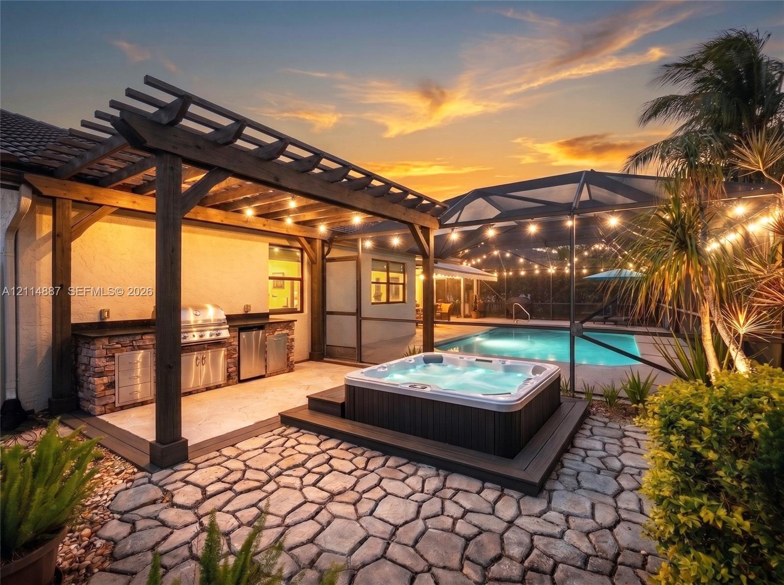 Outdoor kitchen featuring a stone-veneer base and stainless steel built-in grill, cedar-finish pergola, integrated spa, and a screened-in pool area with paver patio