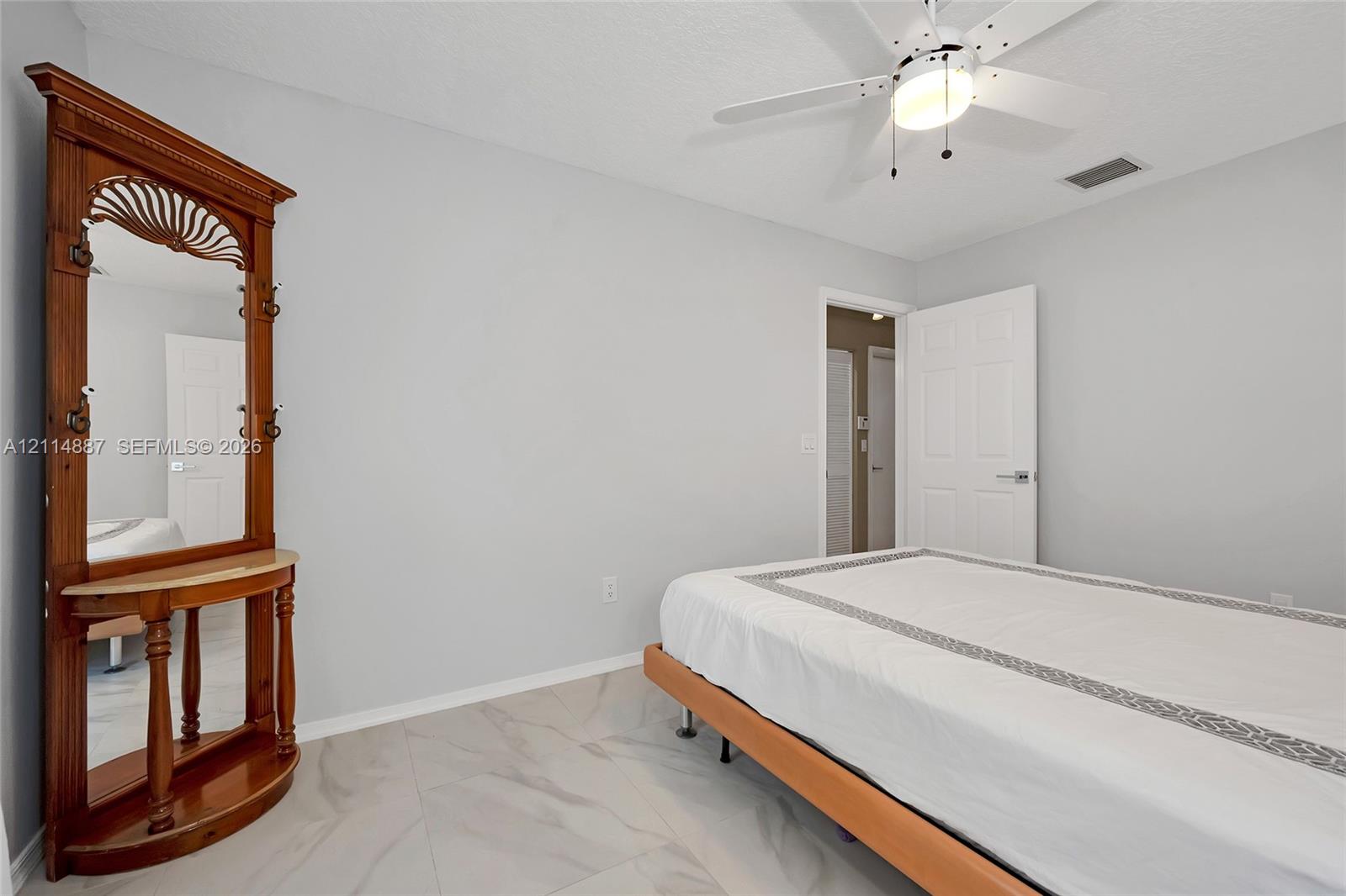 Neutral-toned interior space featuring light-colored stone-finish tile flooring, white-painted walls, and a ceiling-mounted fan with integrated lighting