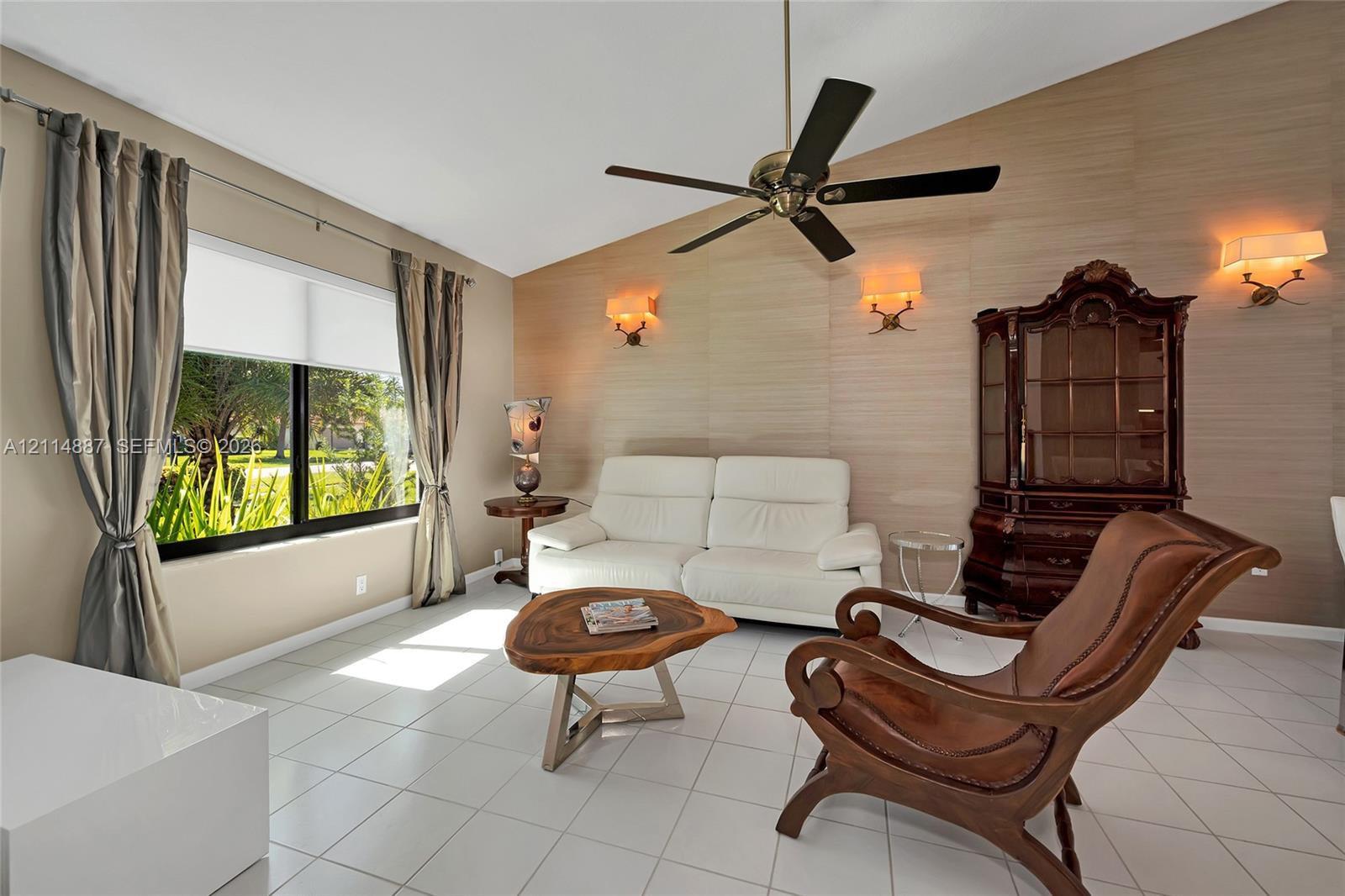 Vaulted ceiling with a central multi-blade ceiling fan, textured accent wall, polished tile flooring, and wall-mounted sconce lighting