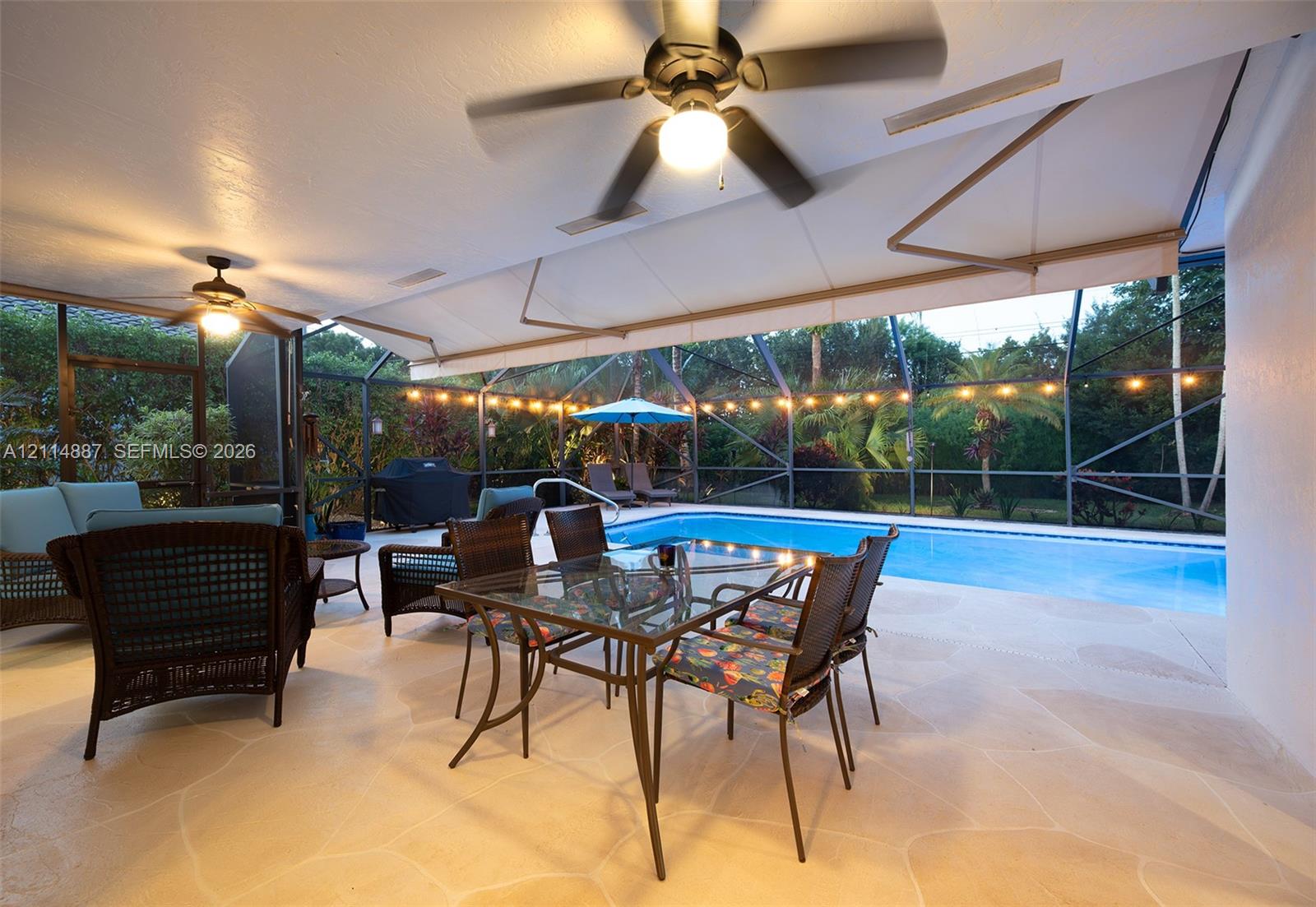Covered lanai featuring paver flooring, dual ceiling fans, retractable awning, and screen enclosure over a swimming pool