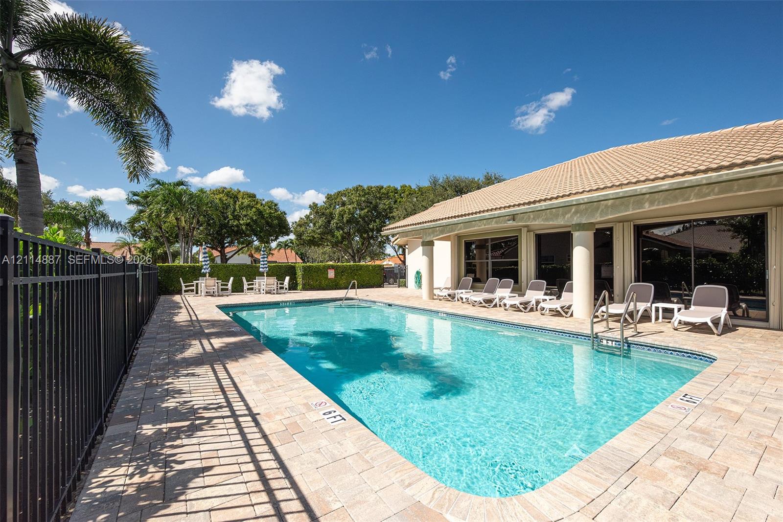 Rectangular swimming pool featuring a brick-paver deck, perimeter black metal fencing, and integrated pool steps under a covered patio area